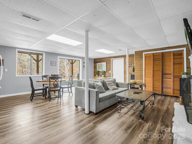 living room with a drop ceiling, hardwood / wood-style flooring, and wooden walls