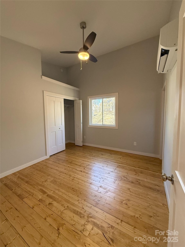 unfurnished bedroom featuring a closet, ceiling fan, a wall unit AC, and light hardwood / wood-style floors