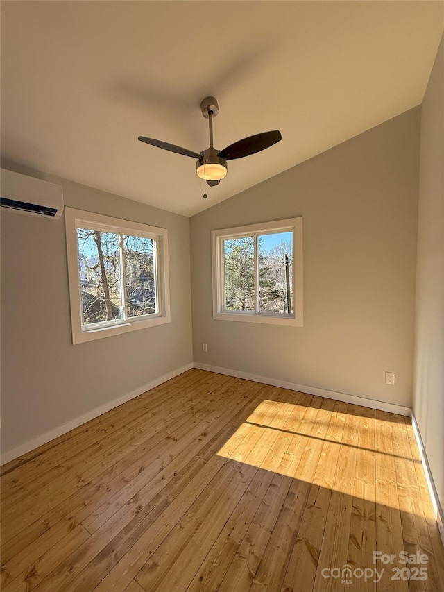 spare room featuring vaulted ceiling, light hardwood / wood-style floors, an AC wall unit, and ceiling fan