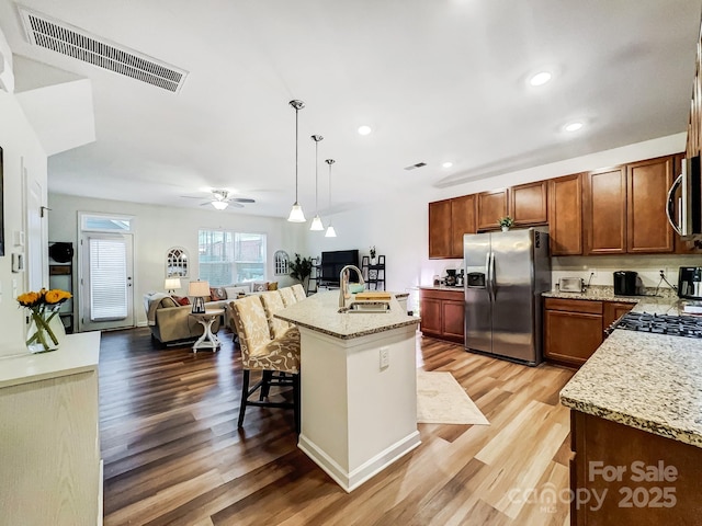 kitchen with sink, a breakfast bar area, decorative light fixtures, stainless steel appliances, and a kitchen island with sink