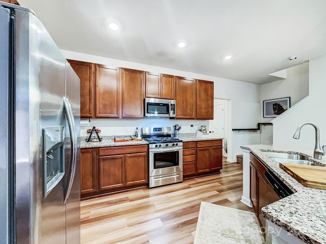 kitchen with appliances with stainless steel finishes, light stone countertops, sink, and light hardwood / wood-style flooring