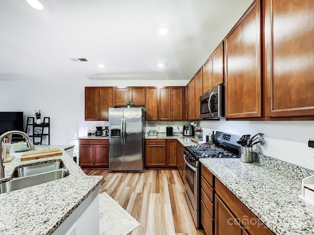 kitchen featuring light stone counters, sink, light wood-type flooring, and appliances with stainless steel finishes