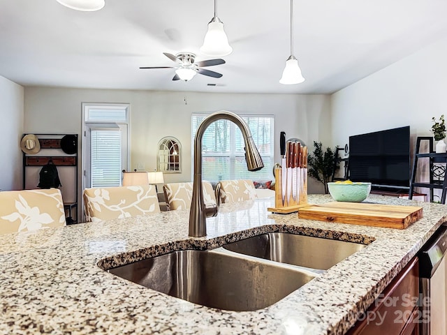 kitchen with sink, dishwasher, ceiling fan, light stone counters, and decorative light fixtures