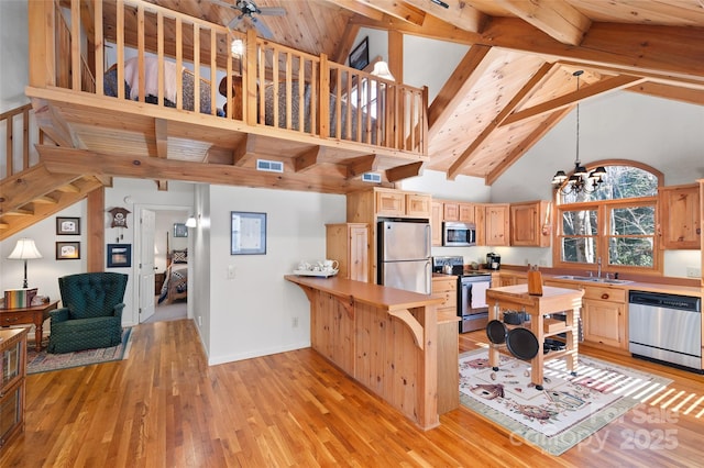 kitchen featuring appliances with stainless steel finishes, decorative light fixtures, light hardwood / wood-style floors, kitchen peninsula, and light brown cabinets