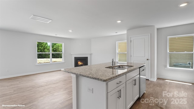 kitchen featuring sink, light stone counters, white cabinets, a center island with sink, and light wood-type flooring