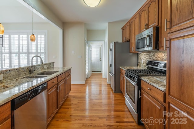 kitchen featuring sink, backsplash, stainless steel appliances, light stone countertops, and light wood-type flooring