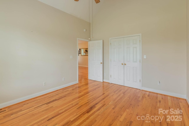 unfurnished bedroom featuring ceiling fan, high vaulted ceiling, a closet, and light wood-type flooring