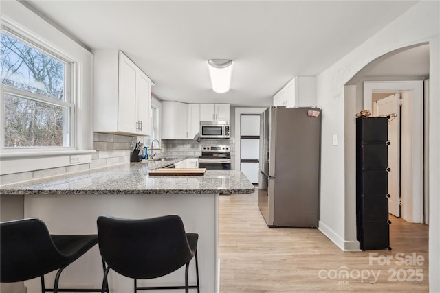 kitchen featuring a breakfast bar, white cabinets, kitchen peninsula, stainless steel appliances, and light stone countertops