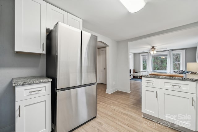 kitchen with white cabinetry, light stone counters, light hardwood / wood-style flooring, stainless steel refrigerator, and ceiling fan