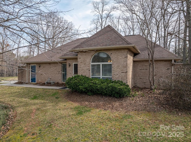 view of front of home with brick siding, a front lawn, and roof with shingles