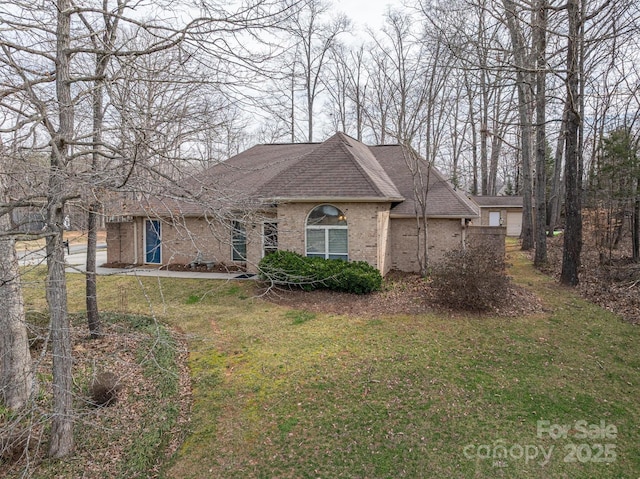 view of front of home featuring a shingled roof, a front yard, and brick siding