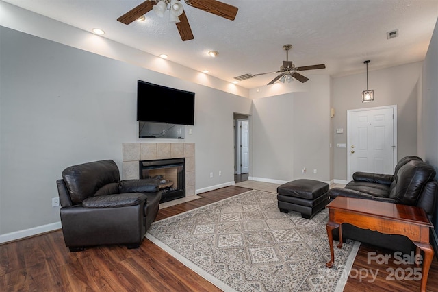 living room featuring a tile fireplace, wood finished floors, visible vents, and baseboards