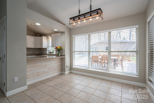 kitchen featuring light tile patterned floors, baseboards, vaulted ceiling, white cabinetry, and a sink