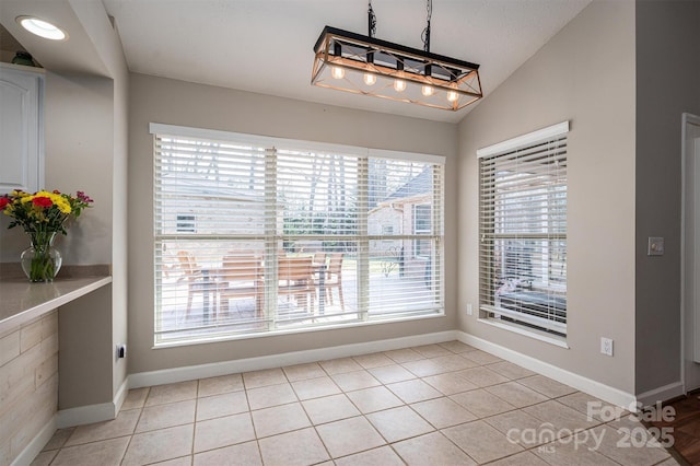 unfurnished dining area featuring light tile patterned floors, baseboards, and vaulted ceiling