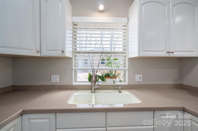 kitchen with light countertops, a sink, white cabinetry, and a healthy amount of sunlight