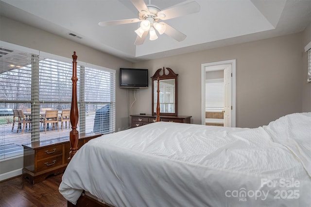 bedroom with a ceiling fan, visible vents, a raised ceiling, and dark wood-type flooring