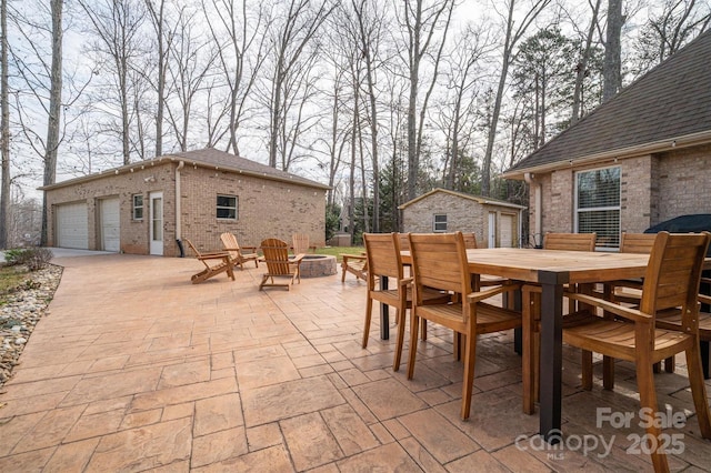 view of patio featuring a garage, an outdoor fire pit, outdoor dining area, and an outbuilding