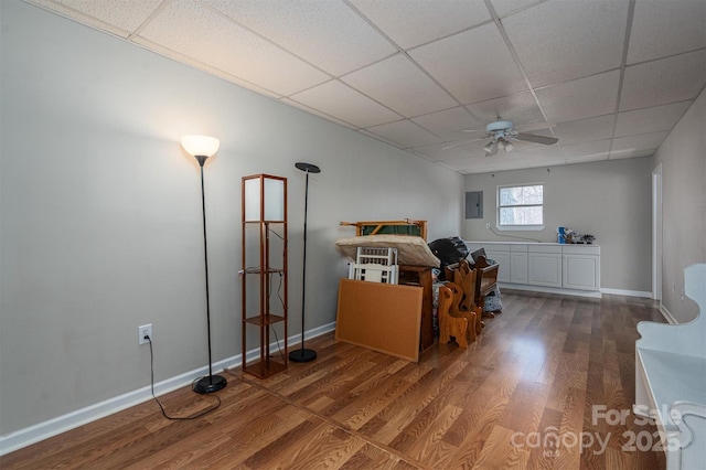 interior space featuring a paneled ceiling, electric panel, baseboards, and wood finished floors