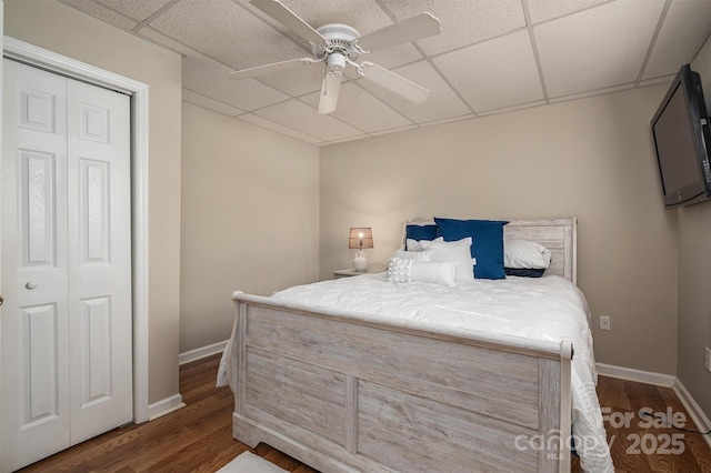 bedroom with dark wood-style floors, ceiling fan, a drop ceiling, and baseboards