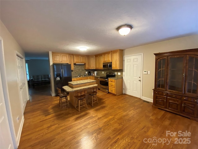 kitchen featuring appliances with stainless steel finishes, a kitchen breakfast bar, dark hardwood / wood-style flooring, a kitchen island, and decorative backsplash