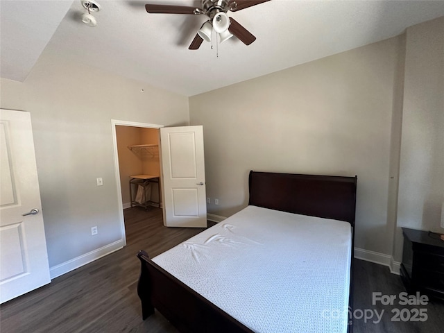 bedroom with dark wood-type flooring, a walk in closet, vaulted ceiling, a closet, and ceiling fan