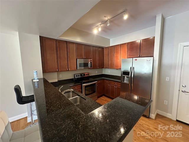 kitchen featuring sink, light hardwood / wood-style flooring, dark stone countertops, appliances with stainless steel finishes, and kitchen peninsula