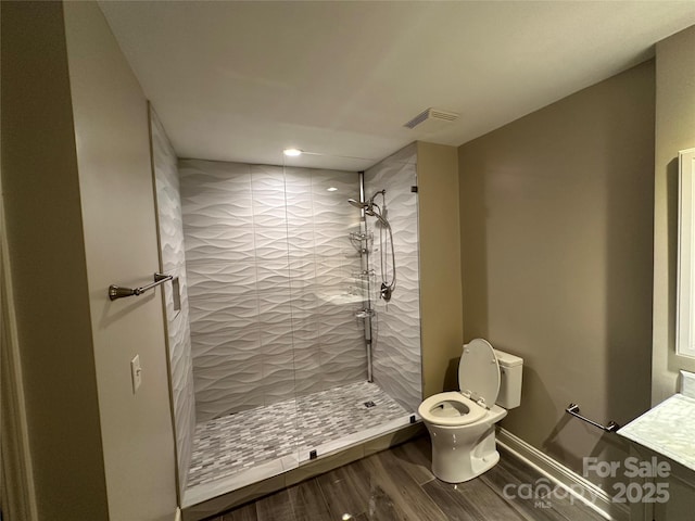 bathroom featuring wood-type flooring, a tile shower, and toilet