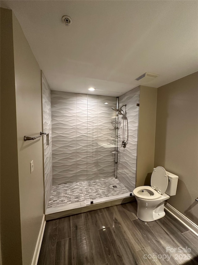 bathroom featuring hardwood / wood-style flooring, tiled shower, and toilet