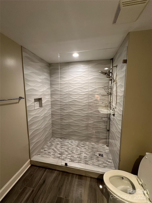 bathroom featuring wood-type flooring, a tile shower, and toilet