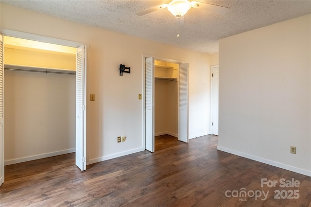 unfurnished bedroom with ceiling fan, dark wood-type flooring, two closets, and a textured ceiling