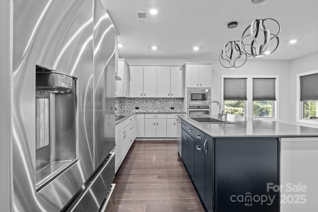 kitchen featuring stainless steel appliances, an island with sink, white cabinets, and decorative light fixtures