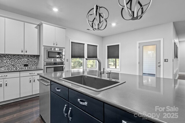 kitchen featuring pendant lighting, sink, white cabinetry, stainless steel appliances, and tasteful backsplash