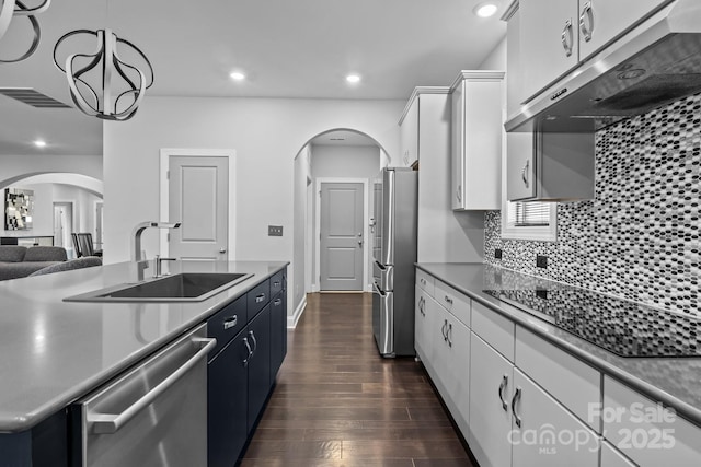 kitchen featuring appliances with stainless steel finishes, range hood, white cabinetry, sink, and hanging light fixtures