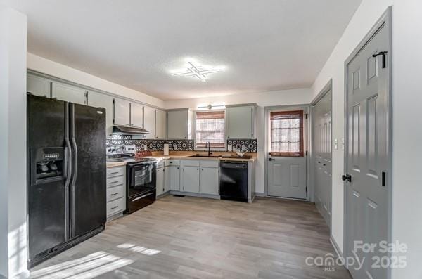 kitchen featuring tasteful backsplash, sink, gray cabinetry, black appliances, and light hardwood / wood-style flooring