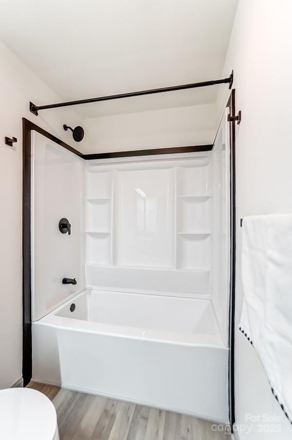 bathroom featuring hardwood / wood-style floors, toilet, and washtub / shower combination