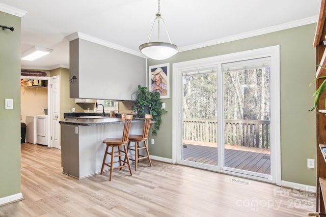 kitchen with a breakfast bar area, crown molding, decorative light fixtures, light hardwood / wood-style flooring, and washing machine and dryer