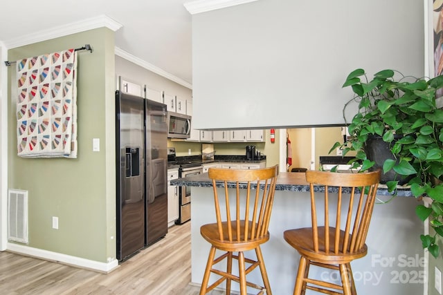 kitchen featuring a kitchen bar, ornamental molding, kitchen peninsula, stainless steel appliances, and white cabinets