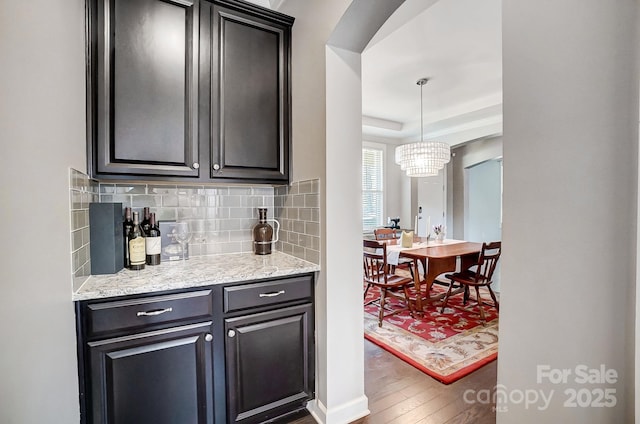 interior space with light stone counters, tasteful backsplash, decorative light fixtures, a raised ceiling, and hardwood / wood-style flooring