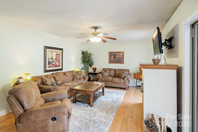 living room featuring ceiling fan, light hardwood / wood-style floors, and a textured ceiling