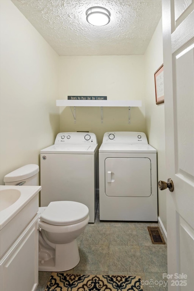 bathroom with vanity, washing machine and dryer, toilet, and a textured ceiling