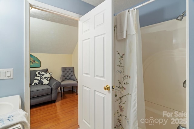 bathroom featuring hardwood / wood-style flooring, lofted ceiling, a shower with shower curtain, and a textured ceiling