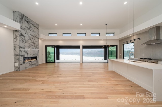 unfurnished living room featuring sink, a towering ceiling, a premium fireplace, and light wood-type flooring