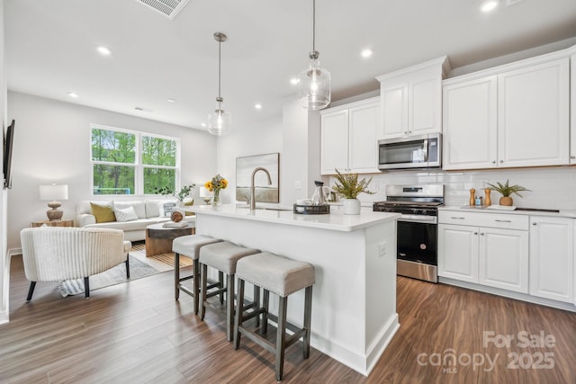 kitchen featuring a breakfast bar, dark wood finished floors, visible vents, a sink, and stainless steel appliances