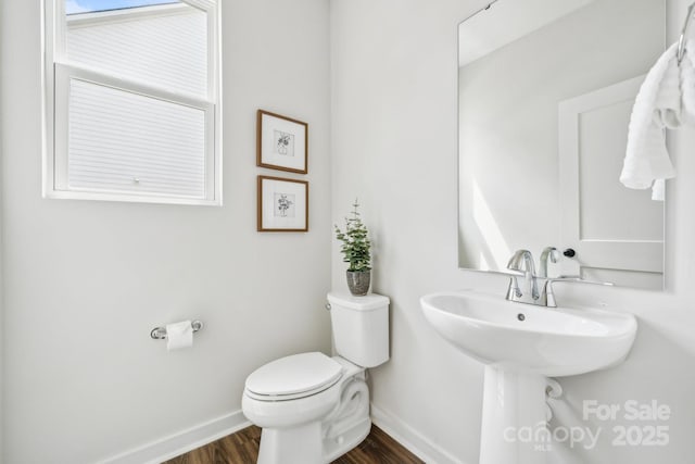 half bathroom featuring a sink, toilet, baseboards, and wood finished floors