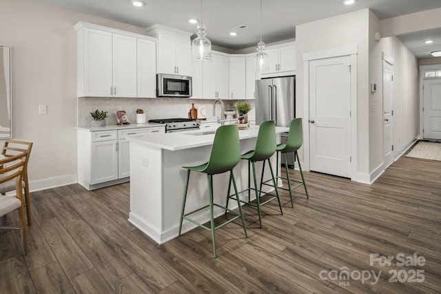 kitchen featuring pendant lighting, white cabinetry, a kitchen island with sink, stainless steel appliances, and a kitchen breakfast bar