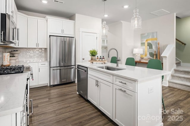 kitchen featuring appliances with stainless steel finishes, dark hardwood / wood-style floors, white cabinets, a center island with sink, and decorative light fixtures