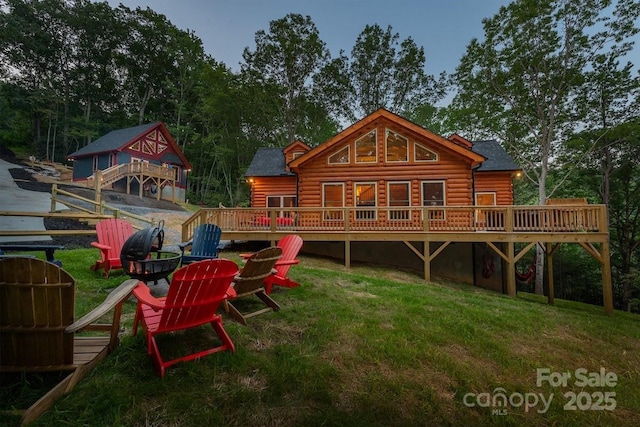 back of property featuring a wooden deck, a lawn, and an outdoor fire pit