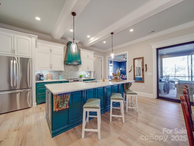 kitchen with white cabinetry, decorative light fixtures, custom range hood, stainless steel appliances, and a kitchen island with sink