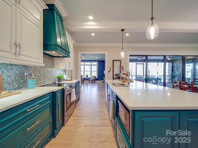 kitchen featuring premium range hood, sink, decorative light fixtures, electric stove, and a kitchen island with sink