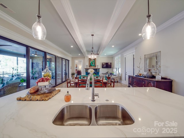 kitchen with light stone counters, sink, ornamental molding, and hanging light fixtures